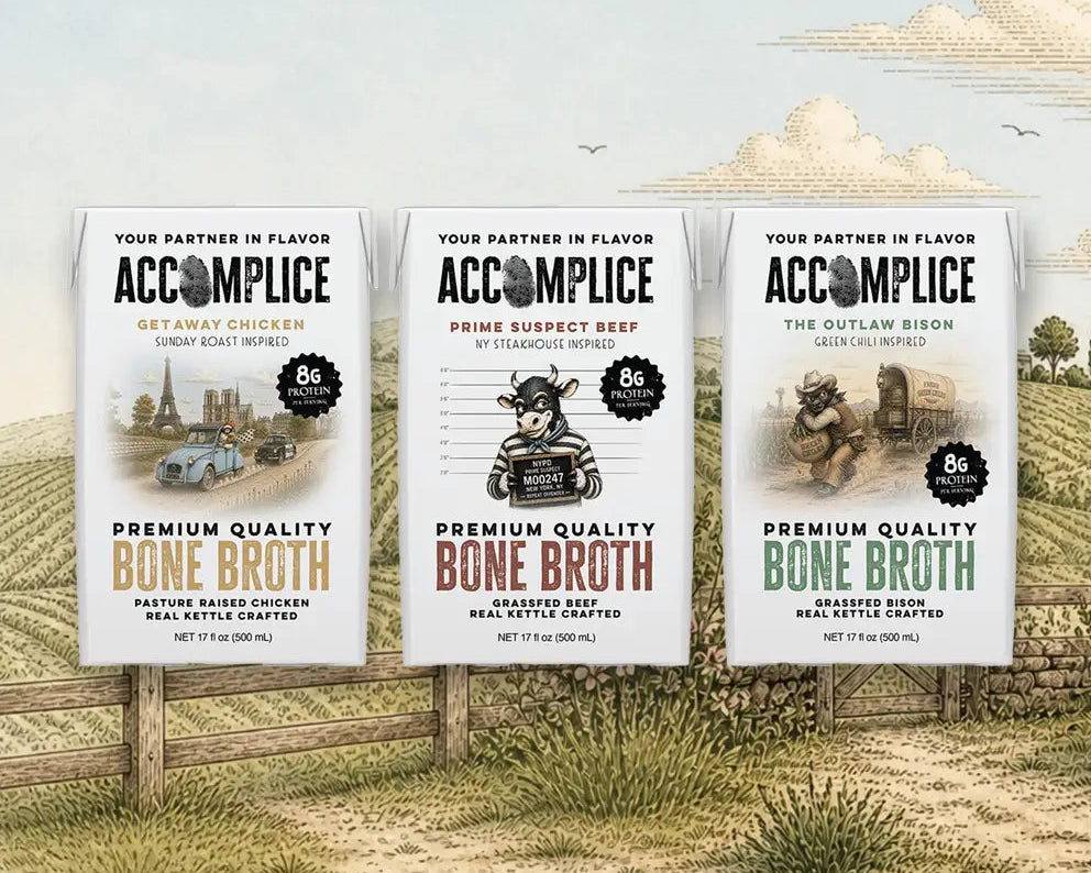Three 'Accomplice' bone broth packages displayed outdoors with a scenic background.